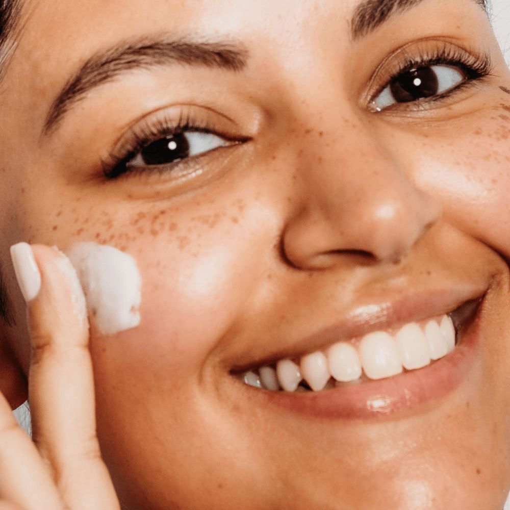 Woman applying cream to her face with a close-up view of her skin texture.
